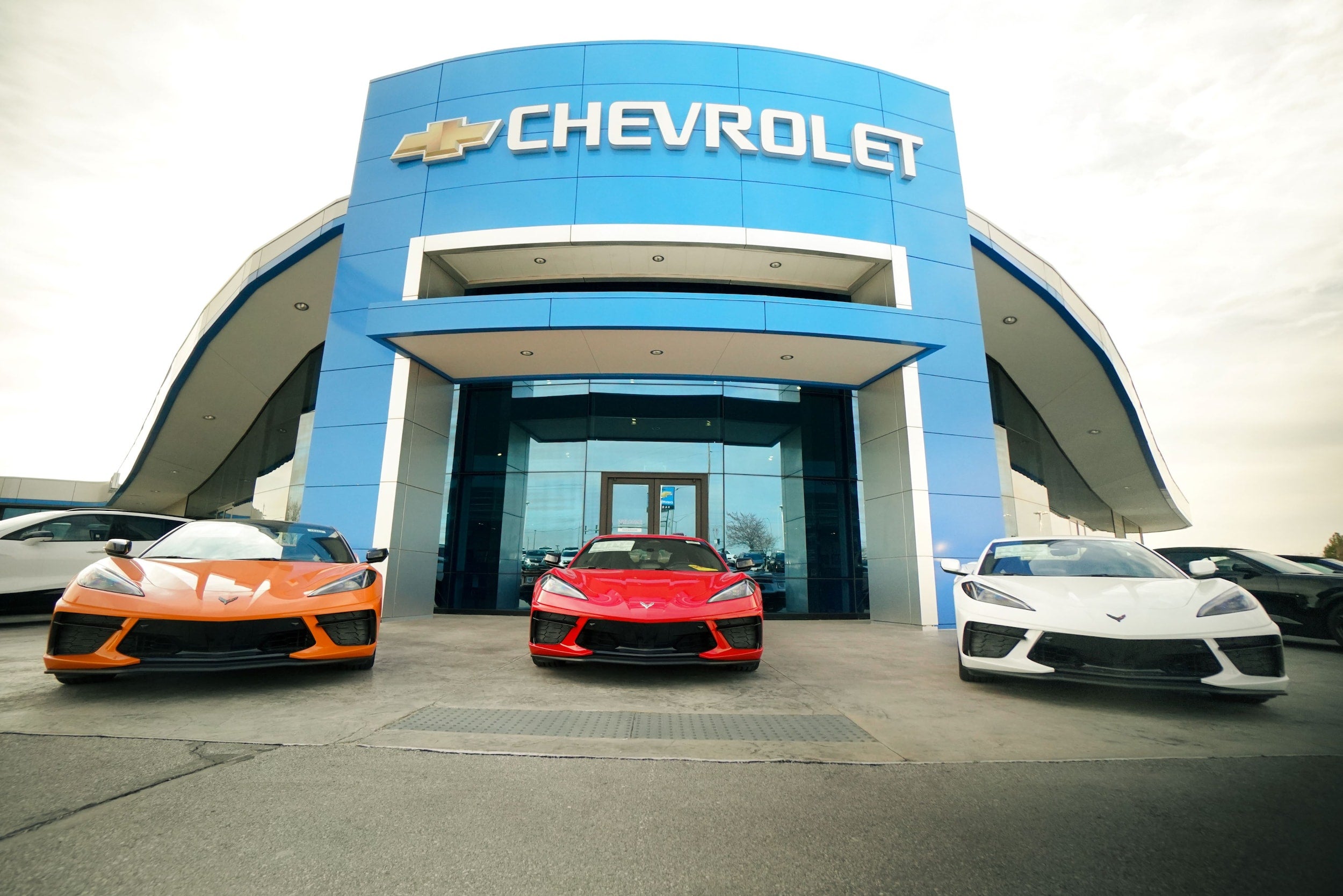 Three new Chevrolet Corvettes parked in front of a blue Chevrolet dealership.